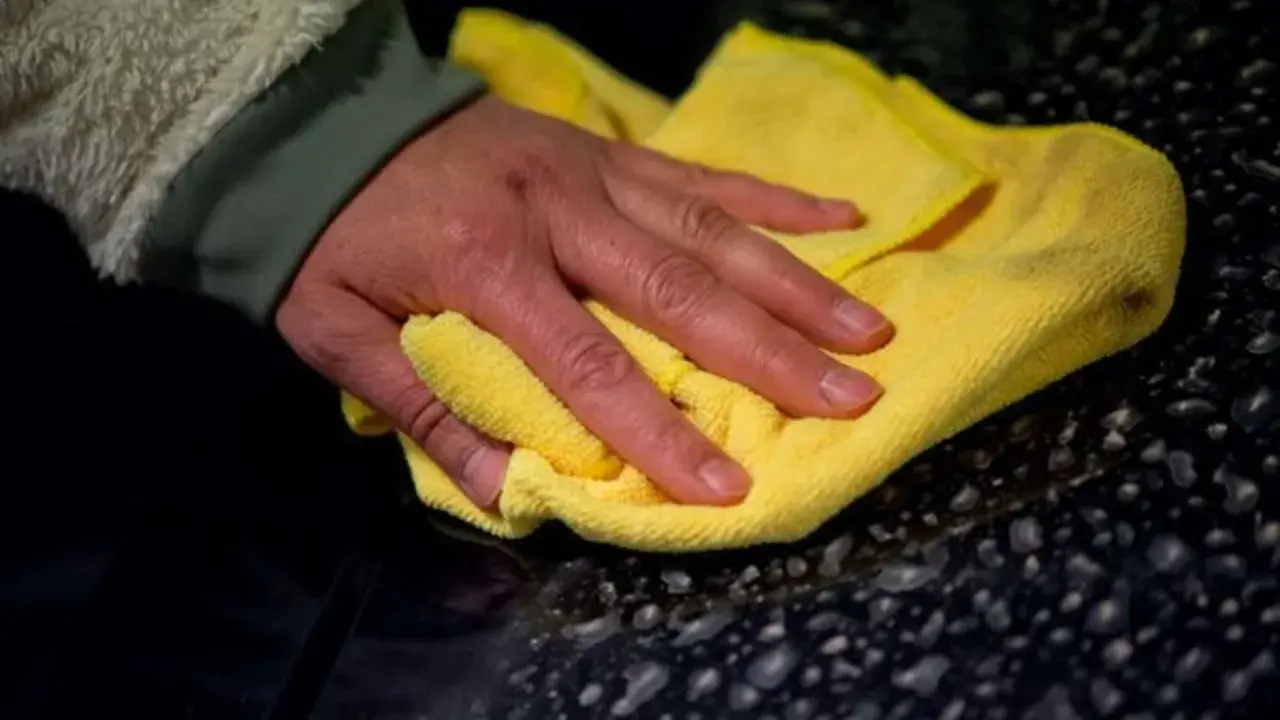 Hand poliert mit gelbem Tuch den dunklen Lack, um das Auto zu polieren und versiegeln.