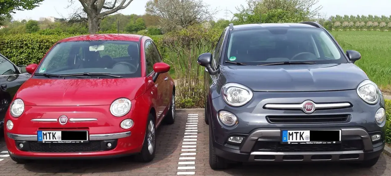 Zwei Fiat 500X, rot und grau, parken nebeneinander. Der graue hat ein paar kleine Probleme, die man auf den ersten Blick nicht sieht.