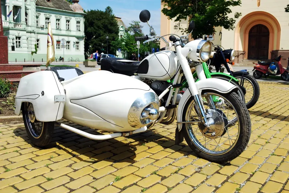 Weiße Motorräder mit Beiwagen und Roller stehen auf einem gelben Kopfsteinpflaster. Ein Helm liegt auf dem Roller, um die Strafe für Fahren ohne Helm zu vermeiden.