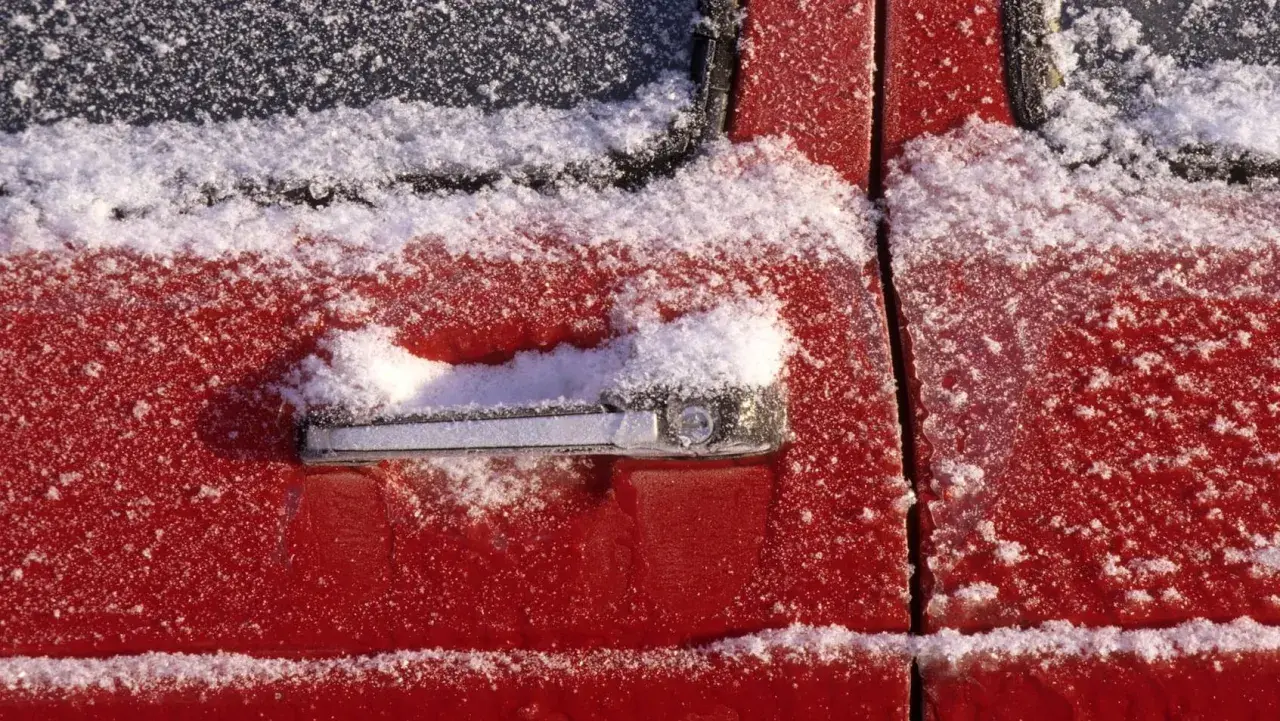 Roter Autolack mit Schnee bedeckt. Wichtig: auto gummi pflegen winter, damit Türen nicht festfrieren.