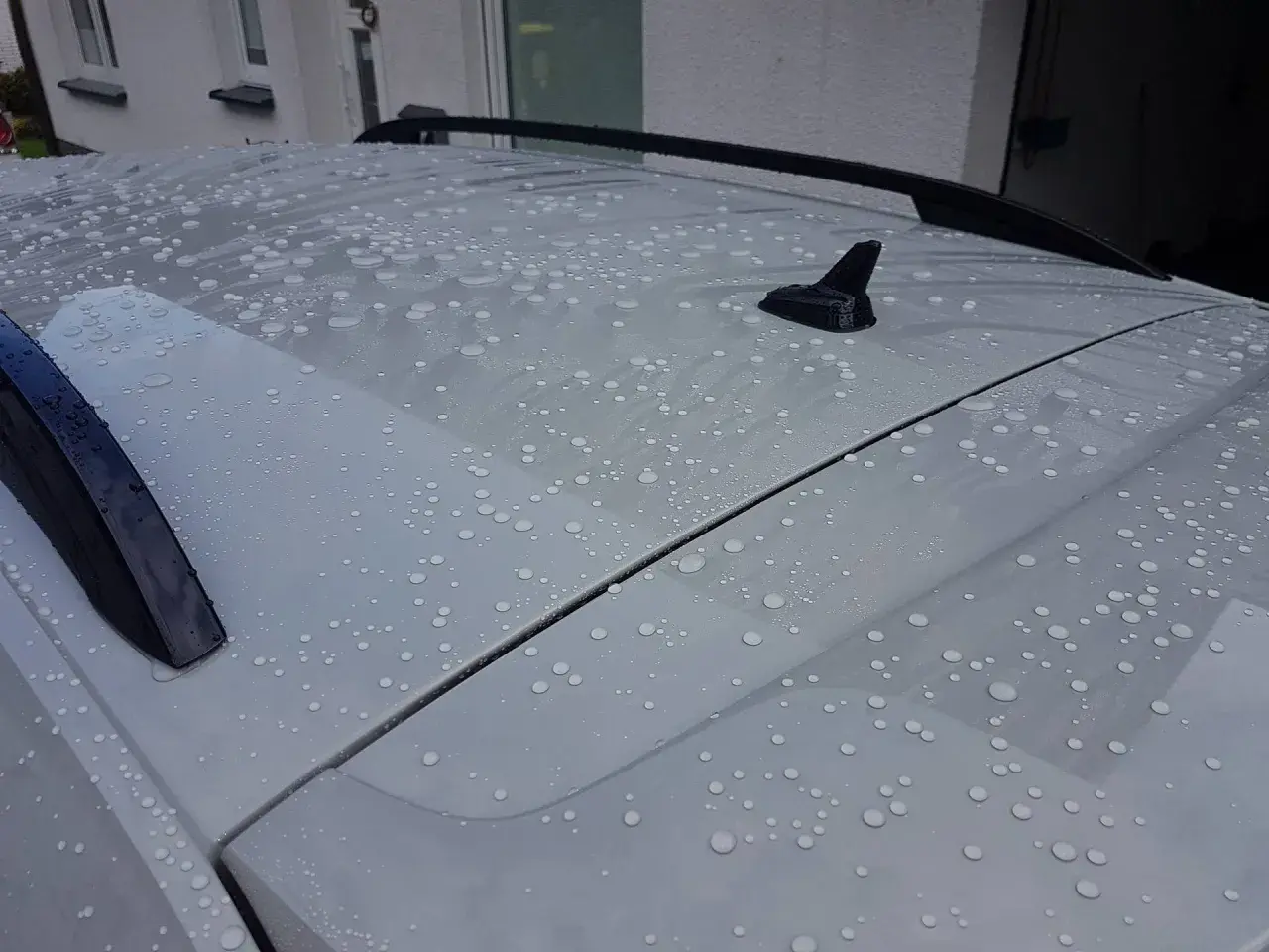 Wassertropfen perlen auf dem Dach eines Autos ab. Ein autoversiegelung test zeigt die wasserabweisende Wirkung.