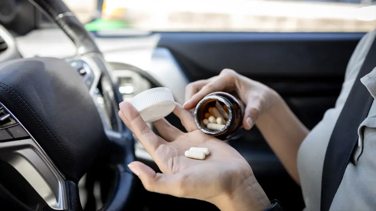 Frau nimmt Ibuprofen im Auto ein. Vorsicht beim Autofahren nach Medikamenteneinnahme.