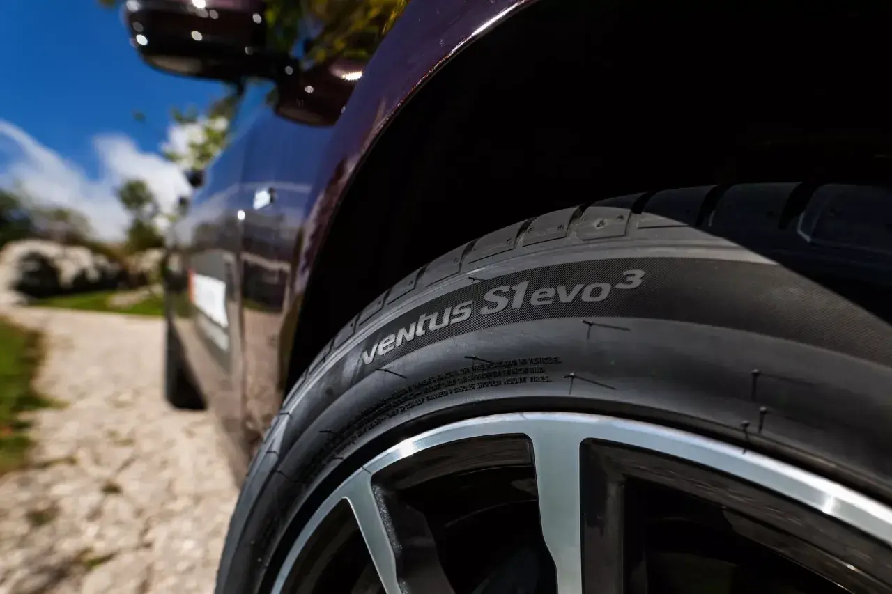 Nahaufnahme eines Hankook Ventus S1 evo 3 Reifens auf einem dunklen Auto, bereit für einen Test auf einer Schotterstraße.