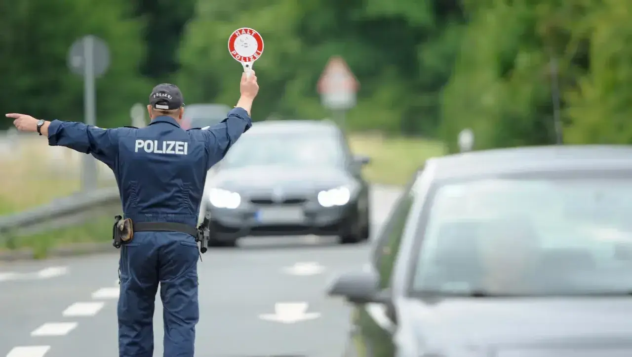 Polizist regelt den Verkehr bei einer allgemeinen Verkehrskontrolle. Er hält ein Stoppschild hoch und winkt Autos weiter.