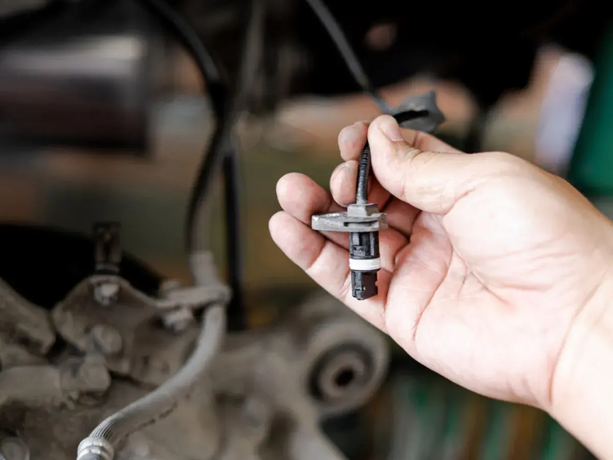 Hand hält ABS-Sensor. Defekter ABS-Sensor Symptome können durch Austausch behoben werden.