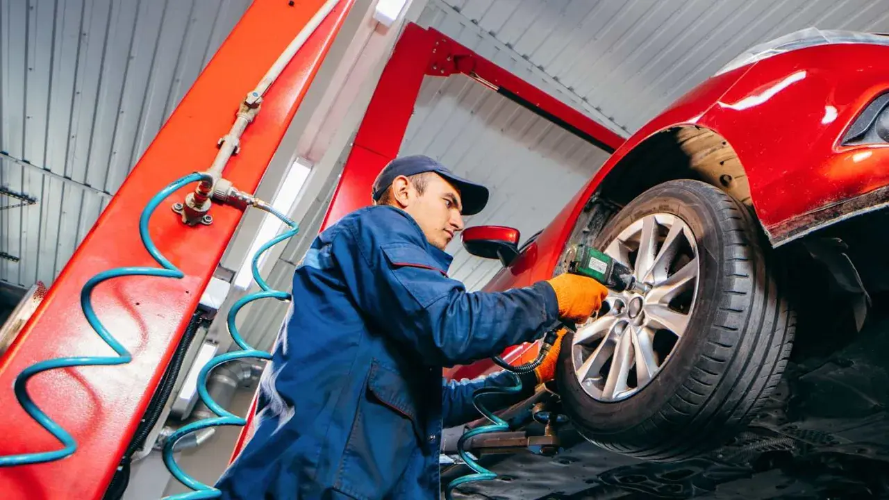 Mechaniker wechselt Reifen am roten Auto. Die Frage "wie lange dauert reifenwechsel" wird hier beantwortet: schnell und effizient.