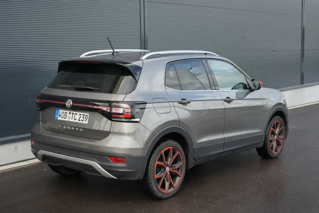 Grauer VW T-Cross mit auffälligen roten Felgen. Hoffentlich gibt es keine vw t-cross probleme, die diese schönen Räder beeinträchtigen.