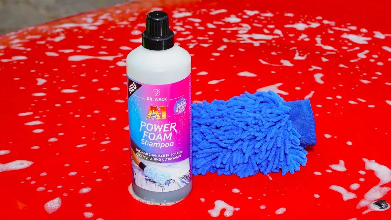 Flasche "A1 Power Foam Shampoo" und blauer Waschhandschuh auf rotem, seifigem Autolack. So gelingt das auto waschen ohne autoshampoo.