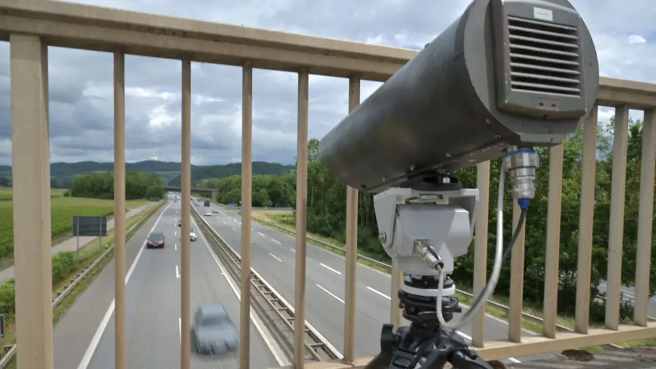 Monocam-Blitzer &uuml;berwacht die Autobahn. Ein graues Ger&auml;t auf einem Stativ blickt auf die vorbeifahrenden Autos.