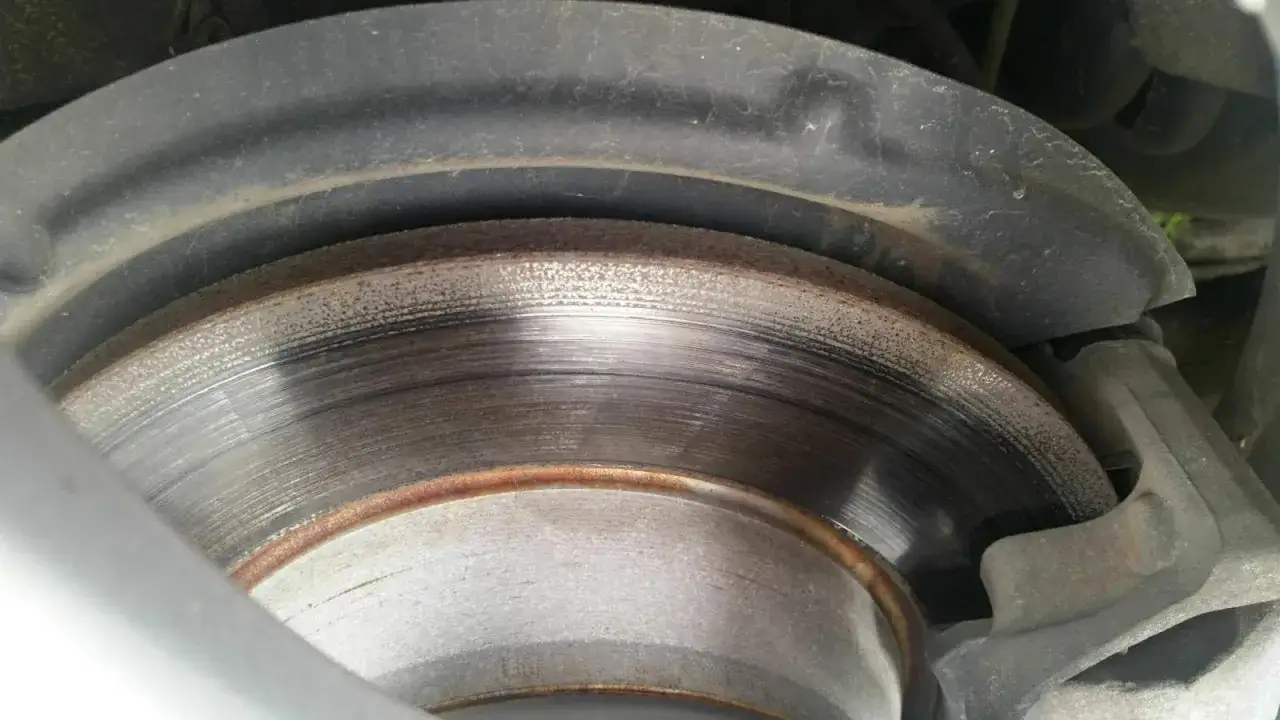 Nahaufnahme einer abgenutzten Bremsscheibe mit sichtbaren Rillen und Rostspuren. Der Bremsbelag ist ebenfalls zu erkennen.