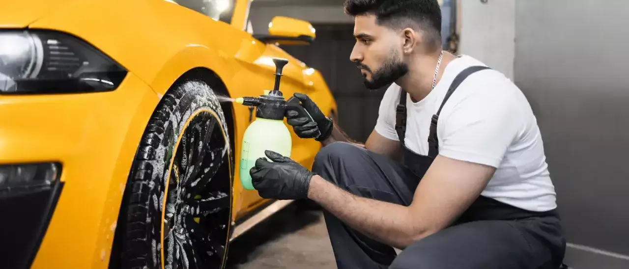Mann mit Handschuhen spr&uuml;ht gelbe Fl&uuml;ssigkeit auf ein gelbes Auto. Ein einfacher felgenreiniger hausmittel f&uuml;r gl&auml;nzende Felgen.