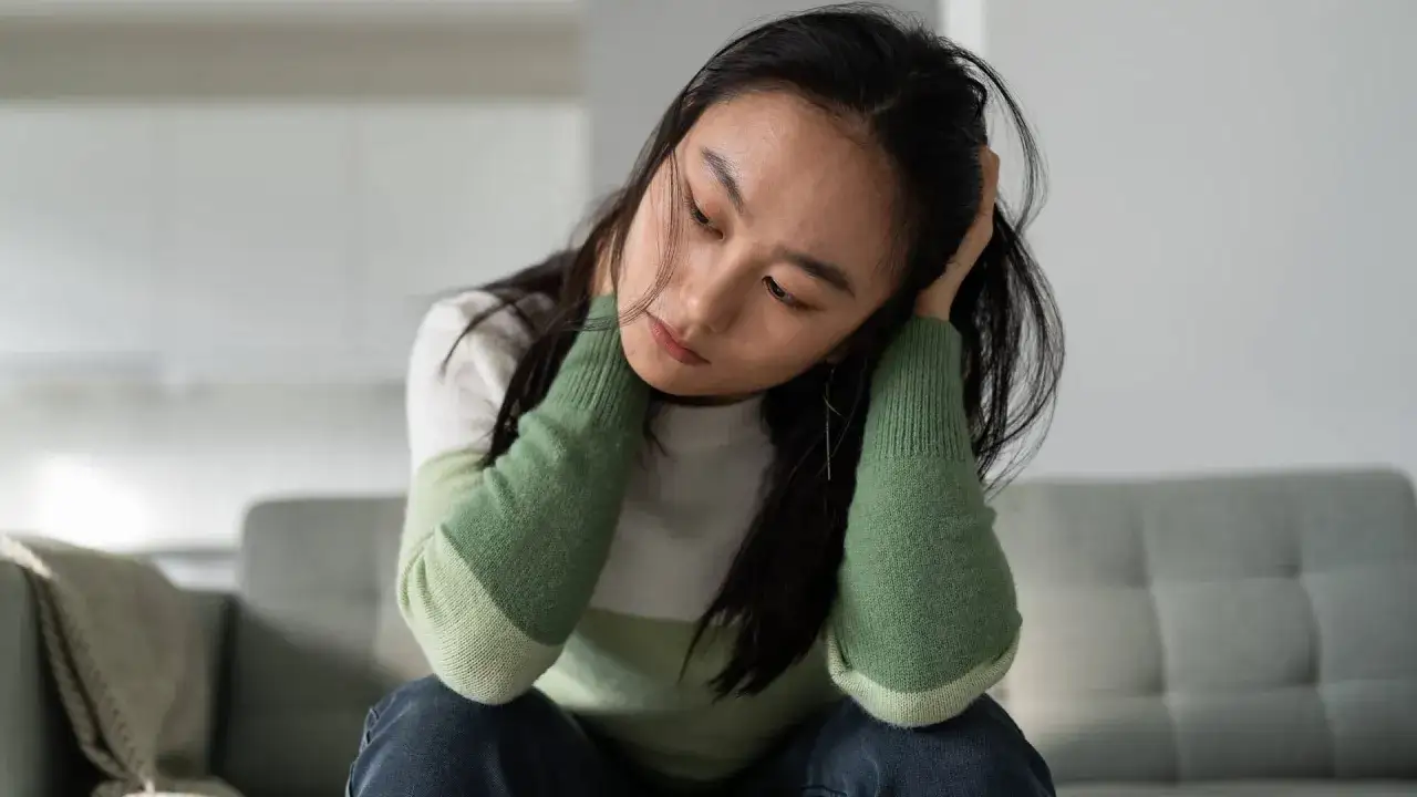 Eine junge Frau sitzt nachdenklich auf einem Sofa. Sie fragt sich, darf man mit Antidepressiva Autofahren?