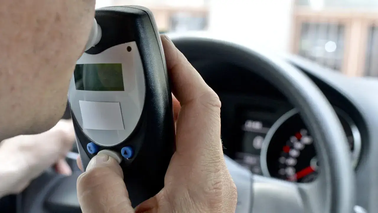 Mann pustet in ein Alkoholmessger&auml;t im Auto. Die Promillegrenze Italien ist wichtig f&uuml;r sicheres Fahren.