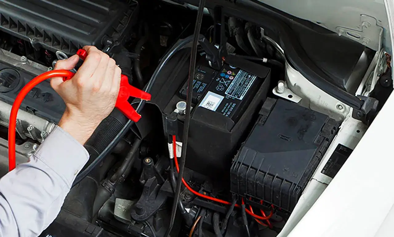 Hand klemmt rote Ladeklemme an Autobatterie. So kann man die Autobatterie laden ohne abklemmen.