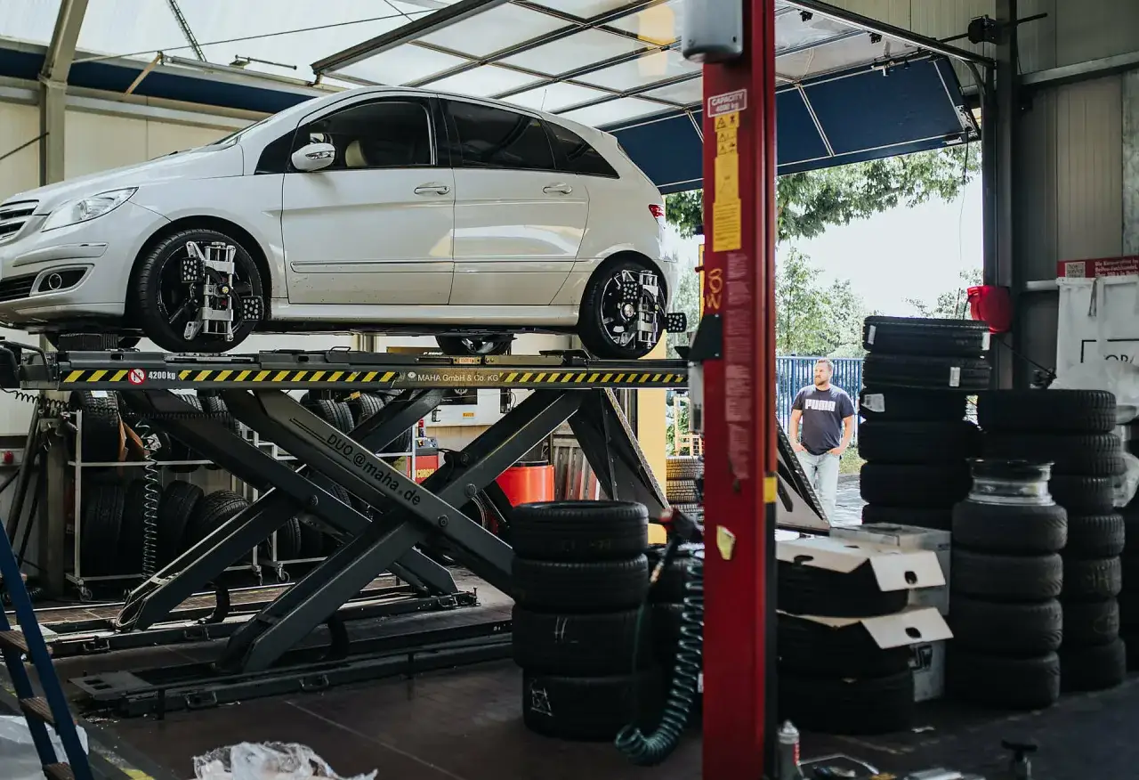 Ein Mann wartet in einer Werkstatt, w&auml;hrend ein Auto auf einer Hebeb&uuml;hne steht. Die Frage 