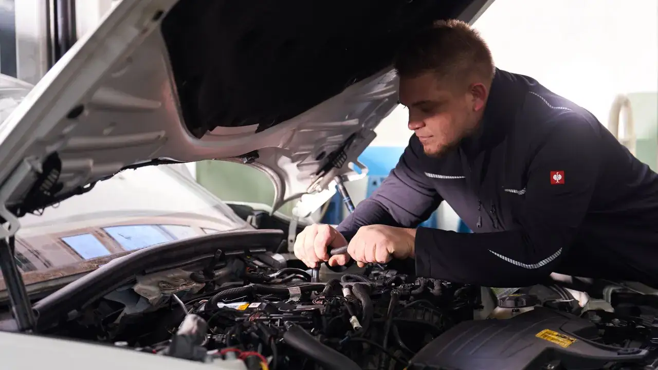 Mechaniker mit Bart arbeitet konzentriert am Motor eines Autos in einer freien Werkstatt.
