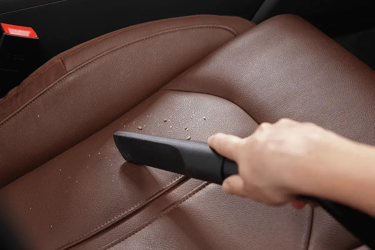 Hand saugt Kr&uuml;mel vom braunen Leder-Autositz. So einfach ist leder reinigen.