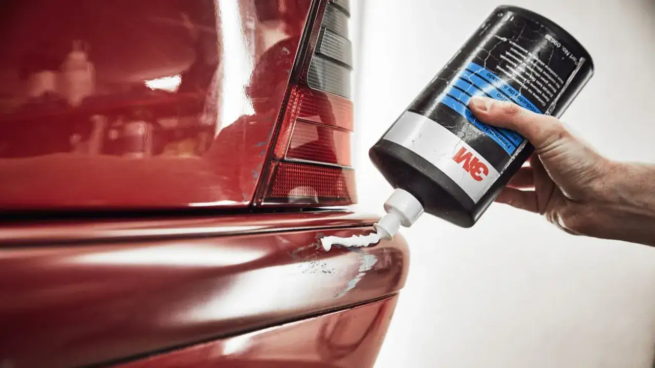 Hand drückt Politur aus 3M-Flasche auf roten Autolack, um Mikrokratzer zu entfernen.