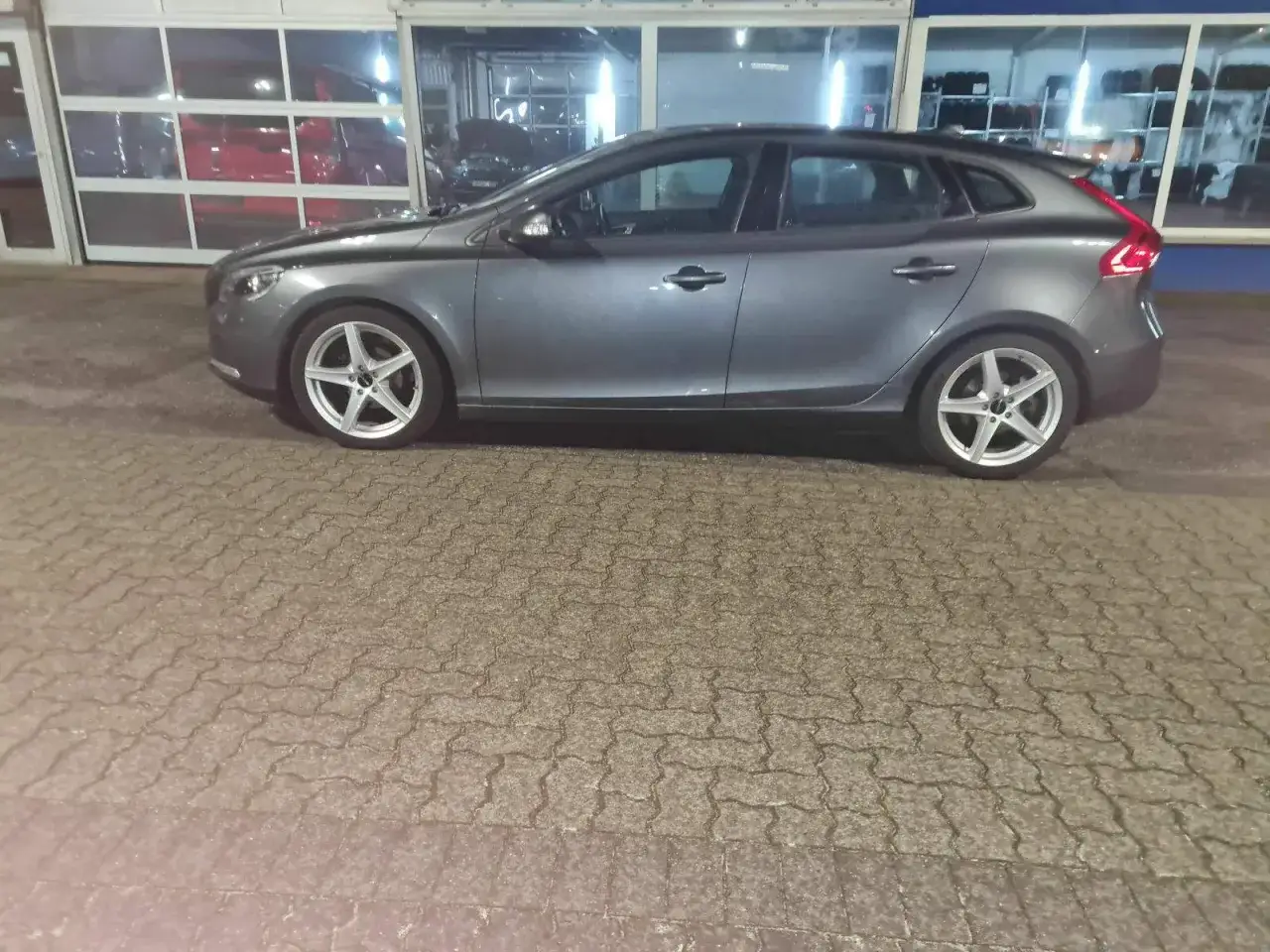 Grauer Volvo V40, der auf einem gepflasterten Hof steht. Mögliche Schwachstellen des Volvo V40 sind hier nicht sichtbar.