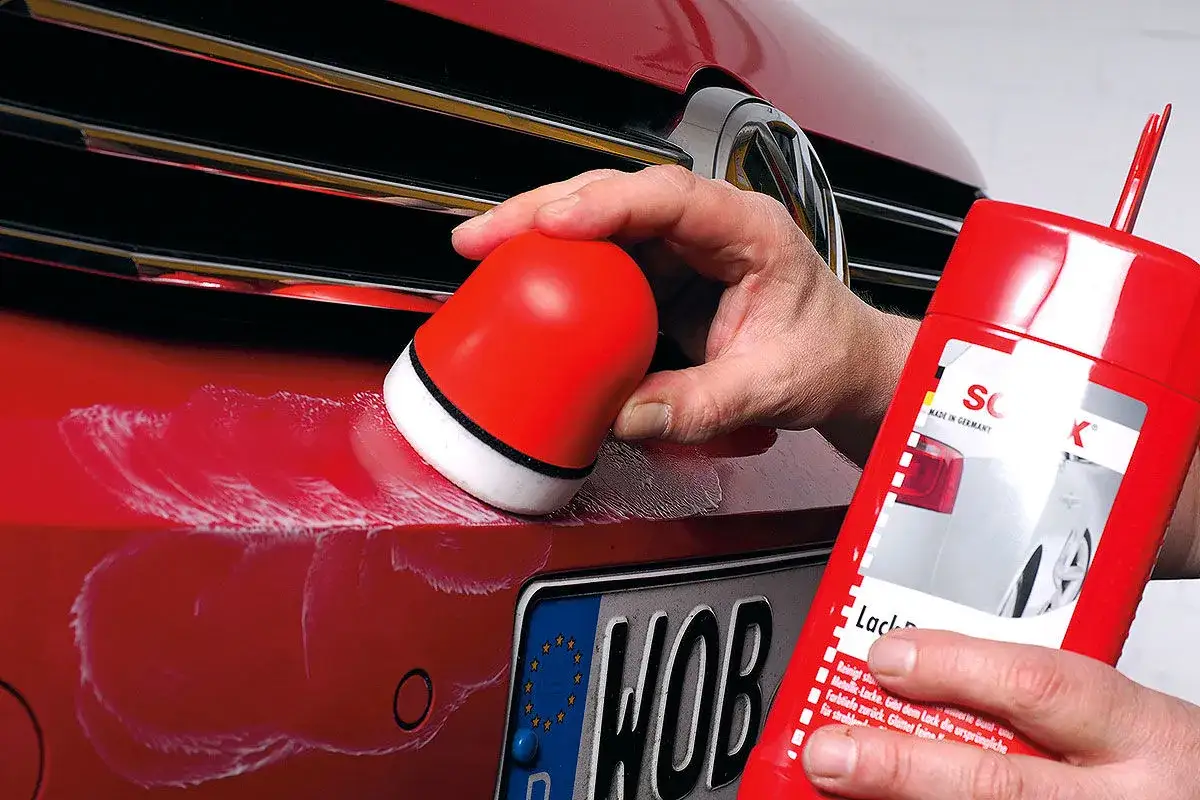 Roter Lack wird mit einem Schwamm und einer roten Flasche gereinigt, um das Auto wachsen ohne polieren zu lassen.