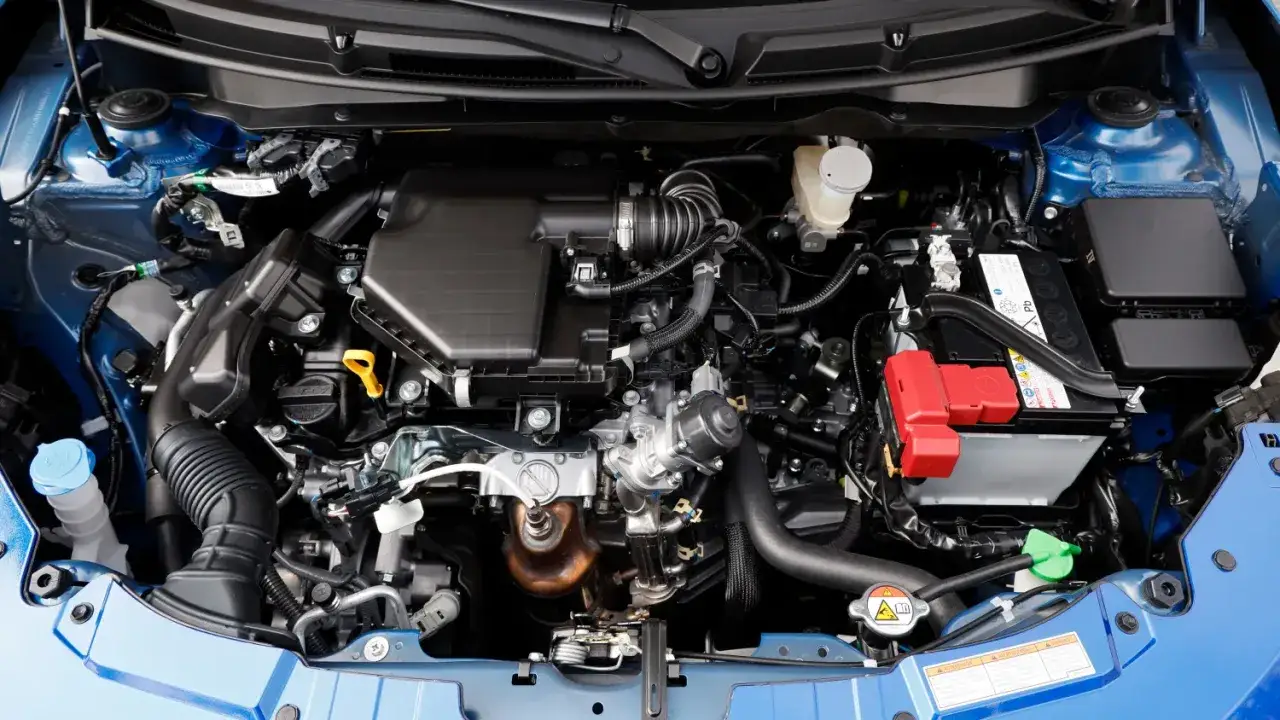 Motorraum eines blauen Suzuki Swift Sport. Viele Kabel und Schl&auml;uche, Batterie und K&uuml;hlmittelbeh&auml;lter sichtbar. Keine offensichtlichen Suzuki Swift Sport Probleme hier.
