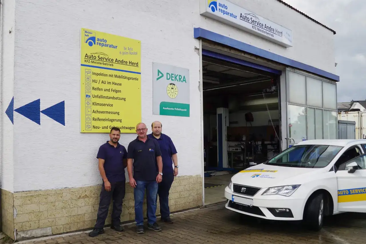 Drei Mechaniker stehen vor ihrer freie Werkstatt. Ein wei&szlig;es Serviceauto mit gelben Streifen steht bereit.