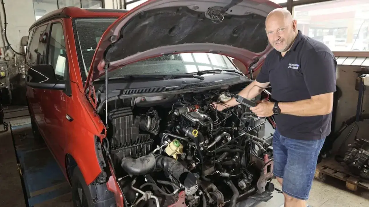 Mechaniker pr&uuml;ft den Motor eines roten VW T6 mit 150 PS auf Probleme.