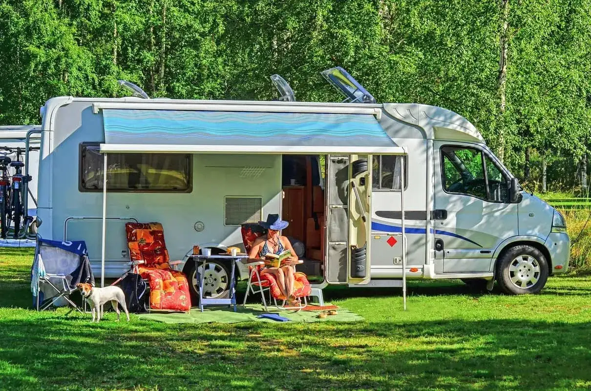 Frau liest unter der ausgefahrenen Wohnmobil Markise, w&auml;hrend ein Hund auf dem Rasen steht. Perfekt f&uuml;r die Wohnmobil Markise reinigen und entspannen.