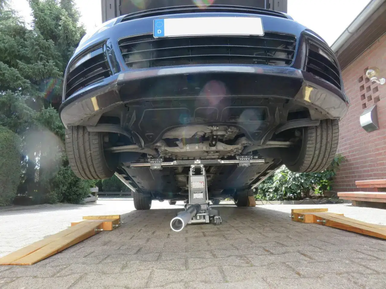 Auto aufbocken: Ein Wagenheber hebt die Vorderseite eines Autos an, um darunter zu arbeiten. Holzkeile sichern die R&auml;der.