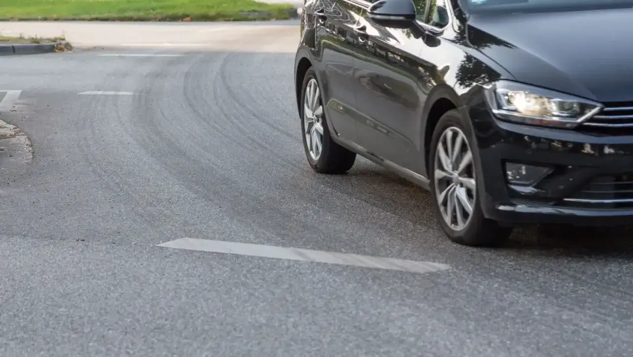 Schwarzes Auto f&auml;hrt eine Kurve, die Reifen quietschen beim Beschleunigen.
