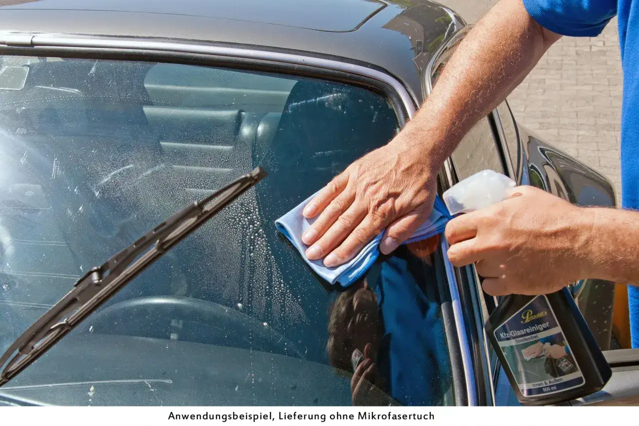 Mann reinigt die Windschutzscheibe innen streifenfrei mit einem blauen Tuch und Spr&uuml;hflasche.