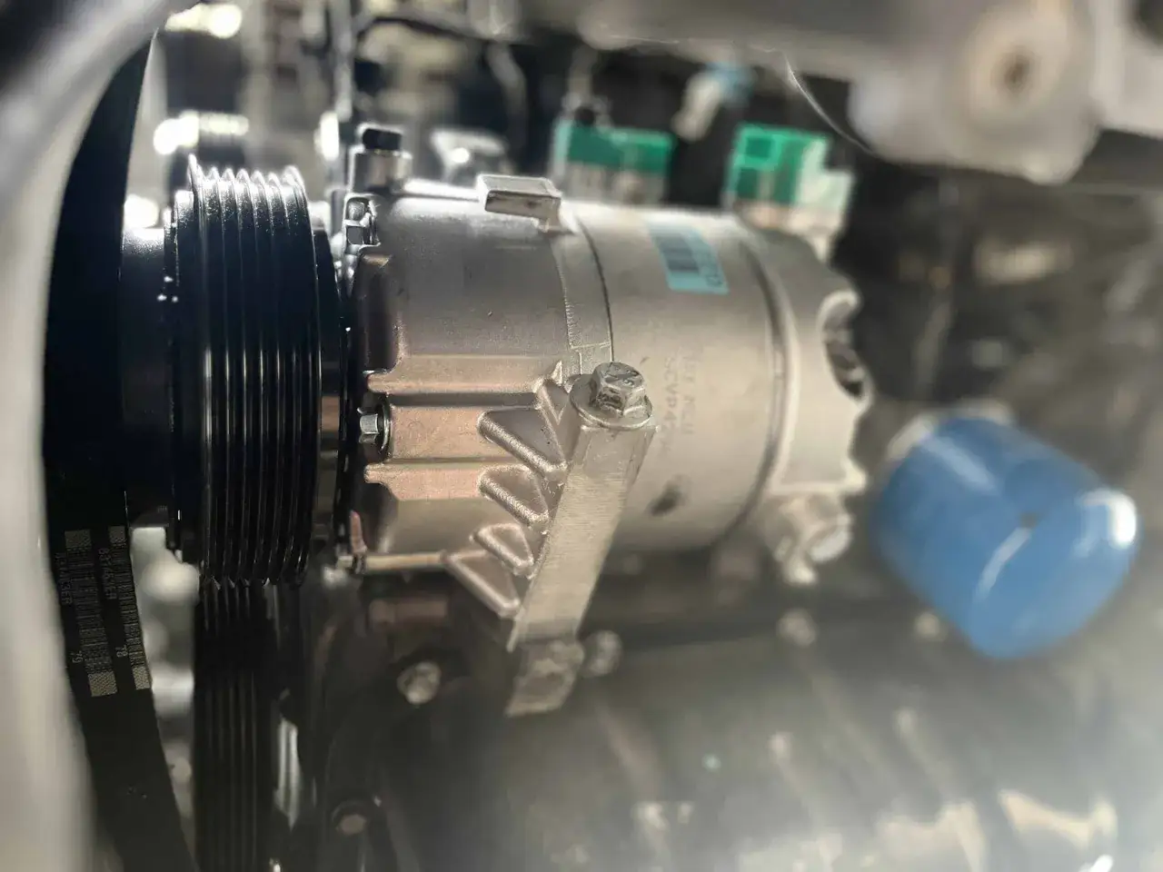 Motorraum mit sichtbarem Klimakompressor. Der Keilriemen ist gespannt, aber der Klimakompressor defekt.
