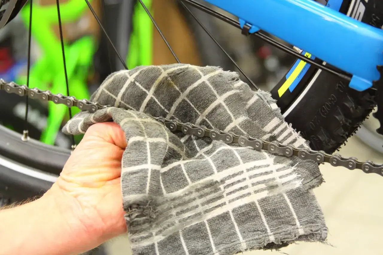 Hand reinigt Fahrradkette mit Tuch. Sorgf&auml;ltige Fahrradpflege f&uuml;r reibungslosen Lauf.