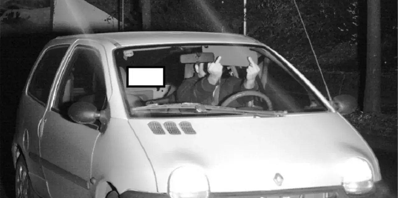 Blitzer Foto: Fahrer eines Kleinwagens zeigt den Mittelfinger, w&auml;hrend er von einer Geschwindigkeitskamera erfasst wird.