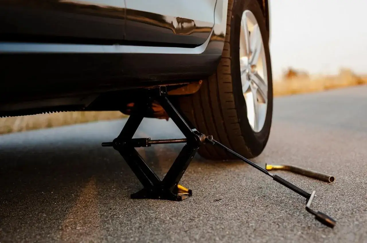 Auto wird mit Wagenheber angehoben, um den Reifen zu wechseln. Die Handbremse ist angezogen, um ein Wegrollen zu verhindern.
