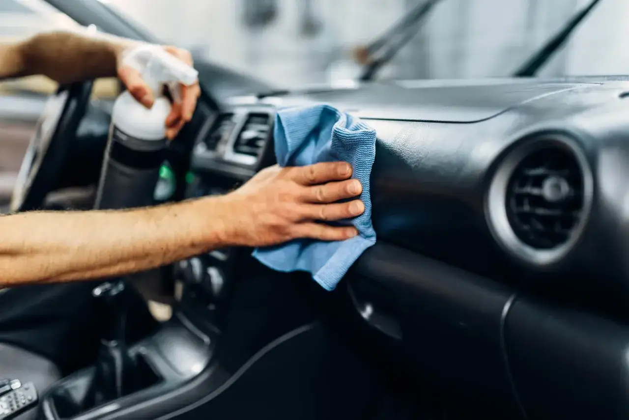 Detailaufnahme: Hände reinigen Armaturenbrett mit blauem Mikrofasertuch und Sprühflasche. Perfekte auto aufbereitung für glänzende Oberflächen.