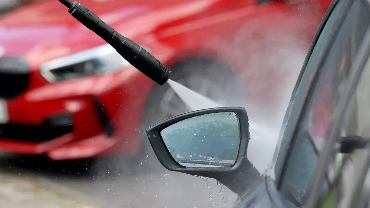 Hochdruckreiniger spr&uuml;ht Wasser auf den Seitenspiegel eines Autos. Vorsicht vor Kratzern durch Waschanlage!