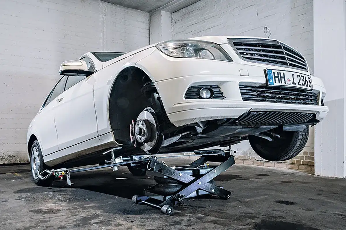 Weißer Mercedes auf Hebebühne, Reifenwechsel steht an. Informieren Sie sich über die reifenwechsel kosten.