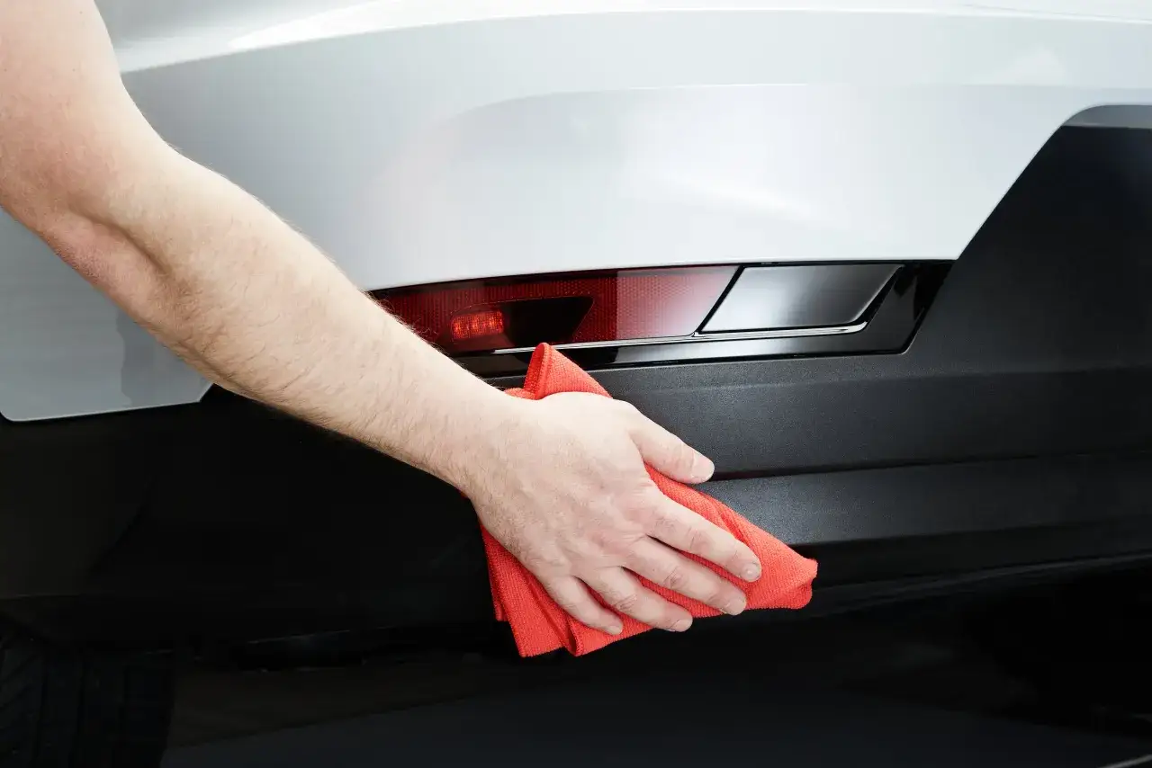 Hand poliert und versiegelt den wei&szlig;en Kotfl&uuml;gel eines Autos mit einem roten Mikrofasertuch.