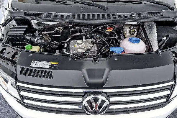 VW T6 150 PS Motorraum mit sichtbaren Leitungen und Kühlmittelbehälter. Mögliche Probleme am Motor sind hier zu sehen.