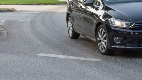 Schwarzes Auto fährt eine Kurve, die Reifen quietschen beim Beschleunigen.