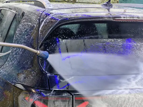 Ein Hochdruckreiniger spritzt Schaum auf ein schwarzes Auto. Die richtige auto waschen reihenfolge sorgt für Glanz.