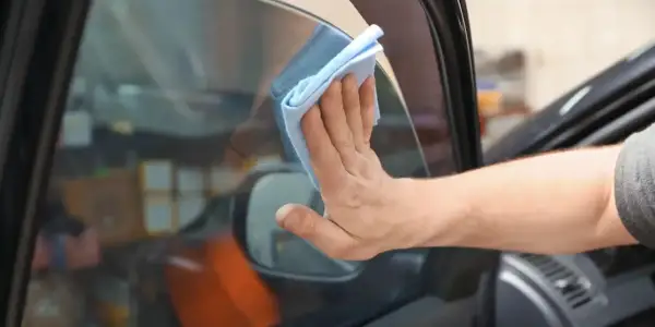 Hand wischt mit blauem Tuch die Windschutzscheibe innen reinigen streifenfrei.