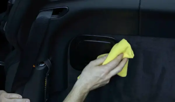 Hand reinigt mit gelbem Tuch den schwarzen Kunststoff im Auto.