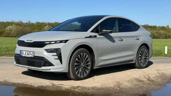 Grauer Skoda Enyaq Coupé auf staubiger Straße, umgeben von grünen Feldern. Manche Fahrer berichten von Skoda Enyaq Problemen, aber dieses Modell scheint unbeeindruckt.