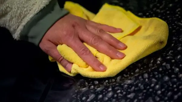 Hand poliert mit gelbem Tuch den dunklen Lack, um das Auto zu polieren und versiegeln.