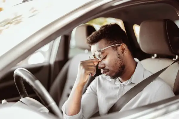 Mann im Auto mit Kopfschmerzen, fragt sich, darf man mit Antidepressiva Autofahren?