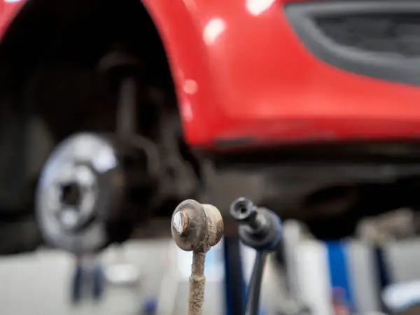 Zwei Koppelstangen liegen vor einem roten Auto. Eine Koppelstange ist defekt und muss ersetzt werden.