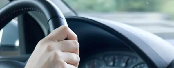 Hand am Lenkrad, das leicht flattert. Die Straße zieht vorbei, ein Gefühl von Bewegung.