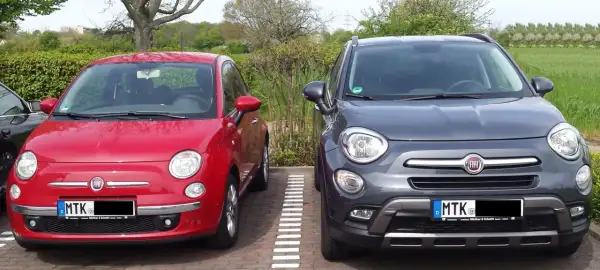 Zwei Fiat 500X, rot und grau, parken nebeneinander. Der graue hat ein paar kleine Probleme, die man auf den ersten Blick nicht sieht.